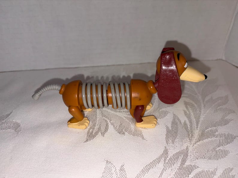 Puede incluir: Un juguete de perro salchicha con un cuerpo en forma de resorte. El perro es principalmente marr&oacute;n con una oreja roja, un hocico beige y patas amarillas. El cuerpo est&aacute; conectado por un resorte gris. Un juguete cl&aacute;sico para ni&ntilde;os.