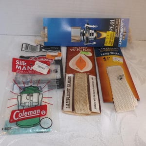 May include: Assortment of oil lamp wicks and parts. Includes packages of wicks from Lamplight Farms, Coleman, and Silk Man. A blue box shows a lamp with the text "Oil Lamp".