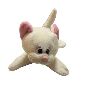 Pode incluir: Um brinquedo de pelúcia branco em forma de gato com orelhas internas rosa e um nariz rosa. O gato tem olhos grandes e pretos e uma boca costurada. O gato está deitado com os braços e as pernas estendidos.