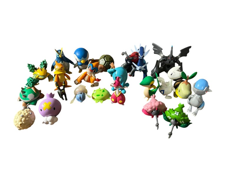May include: A collection of twenty-two small, colorful plastic creature figurines in various shapes and poses. The set includes diverse characters with distinct features such as wings, shells, and spikes, rendered in shades of blue, green, orange, pink, and black.