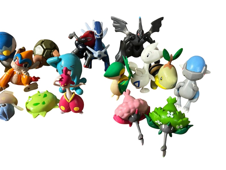 May include: A collection of various small plastic character figurines featuring diverse shapes and colors, including blue, green, pink, orange, and black creatures. The figures display distinct designs with wings, shells, and floral-like elements.
