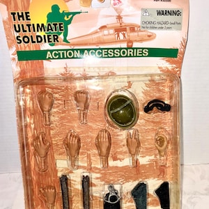 May include: The Ultimate Soldier action accessories set. The set includes various hands, a helmet, goggles, and other accessories. The packaging features a helicopter illustration and the text "Ages 5 & Up".