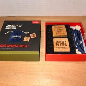 Könnte beinhalten: Ein Holz-Trinkwürfel-Set in einer schwarz-grünen Box mit dem Text "Shake it up, drink it down". Das Set enthält Holzwürfel, einen blauen Kordelzugbeutel und eine rote Box.