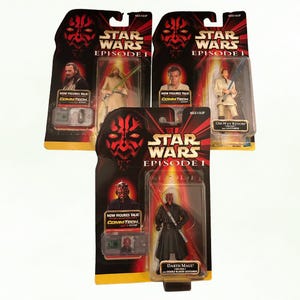 Könnte beinhalten: Drei Star Wars Episode 1 Actionfiguren-Verpackungen. Die Figuren umfassen Obi-Wan Kenobi, Darth Maul und eine weitere Figur. Jede Figur befindet sich in einer transparenten Kunststoffhülle mit einer rot-schwarzen Themenkarte.