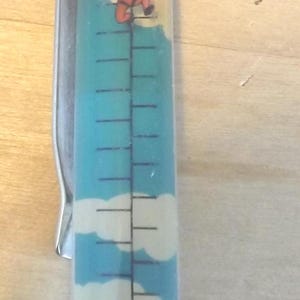 Op de afbeelding: Een novelty pen met een gele dop en basis, een zilveren clip en een transparante barrel. De barrel heeft een blauwe hemel ontwerp met wolken en een cartoon parachutist met de tekst "CARDITEM".