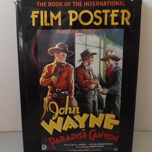 Może przedstawiać: Książka zatytułowana "THE BOOK OF THE INTERNATIONAL FILM POSTER" z plakatem filmowym w stylu vintage. Plakat przedstawia Johna Wayne'a w filmie "Paradise Canyon". Okładka jest czarna z żółtym i czerwonym tekstem, a plakat ma motyw westernu.