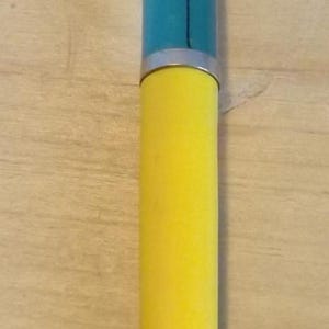 Könnte beinhalten: Ein gelber Stift mit einem silbernen Clip. Der Stiftschaft ist gelb, und der obere Teil hat ein blau-weißes Design mit einer Cartoonfigur. Der Stift liegt auf einer Holzoberfläche.