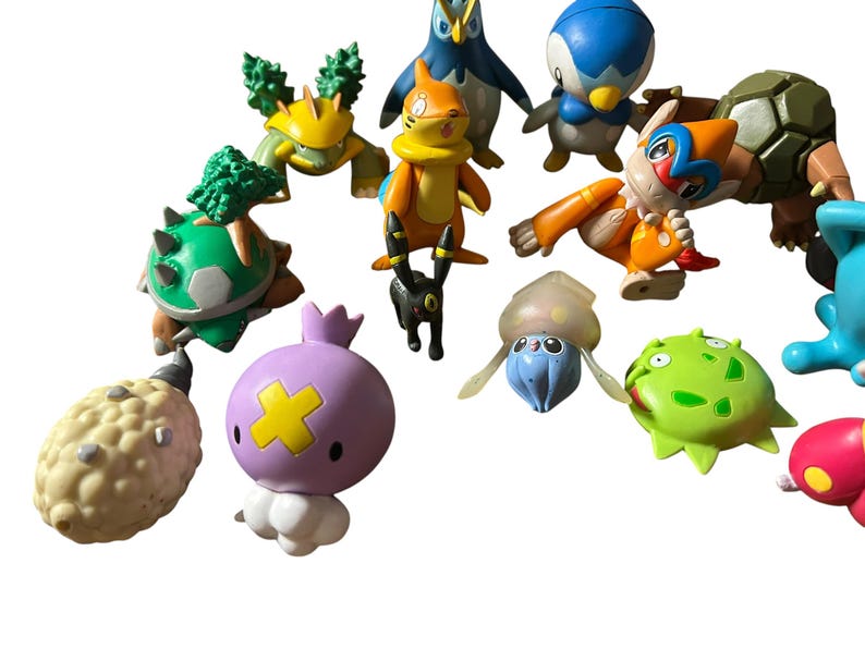 May include: A collection of small plastic character figurines featuring various creatures in colors including orange, green, blue, purple, and beige. The figures display diverse shapes, some with spiky textures, smooth surfaces, and distinct facial features.