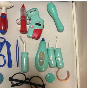 May include: A collection of toy medical tools in various colors. Includes a red and white otoscope, a syringe, a pulse reader, a light green flashlight, blue scissors, tweezers, dental tools, a thermometer, a pair of black glasses, and other accessories.