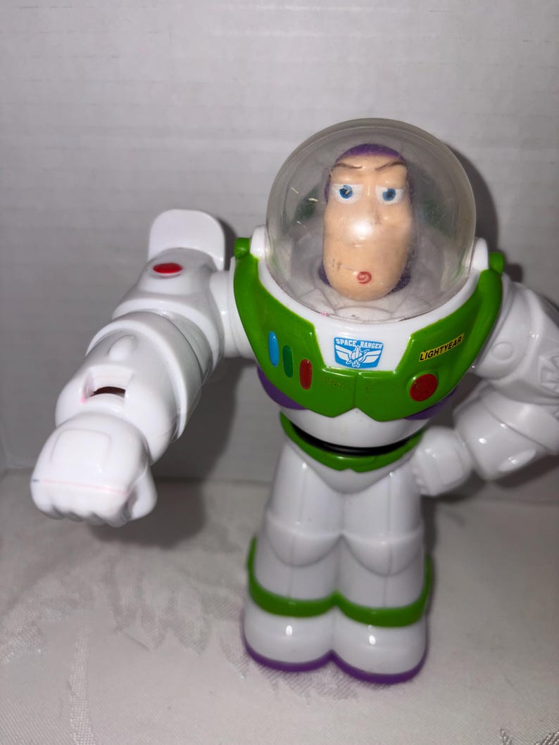 Puede incluir: Figura de acci&oacute;n de Buzz Lightyear de la franquicia Toy Story. La figura es principalmente blanca con detalles verdes y morados. Cuenta con un casco transparente, una placa pectoral verde con las palabras "Space Ranger" y "Lightyear", y brazos articulados.