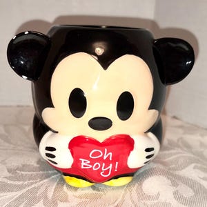 May include: A set of three ceramic mugs with a speckled, matte finish. The mugs are in shades of cream, light gray, and dark gray. Each mug has a simple, minimalist design and a rounded handle.