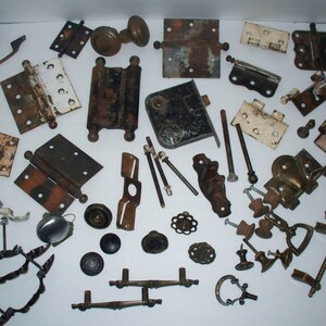 May include: A collection of vintage door hardware, including hinges, knobs, pulls, and plates. The hardware is made of metal and has a variety of finishes, including brass, bronze, and nickel. Some of the pieces are rusty and show signs of wear, while others are in good condition.