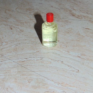 May include: A small, clear glass bottle with a red cap. The bottle is filled with a light yellow liquid.