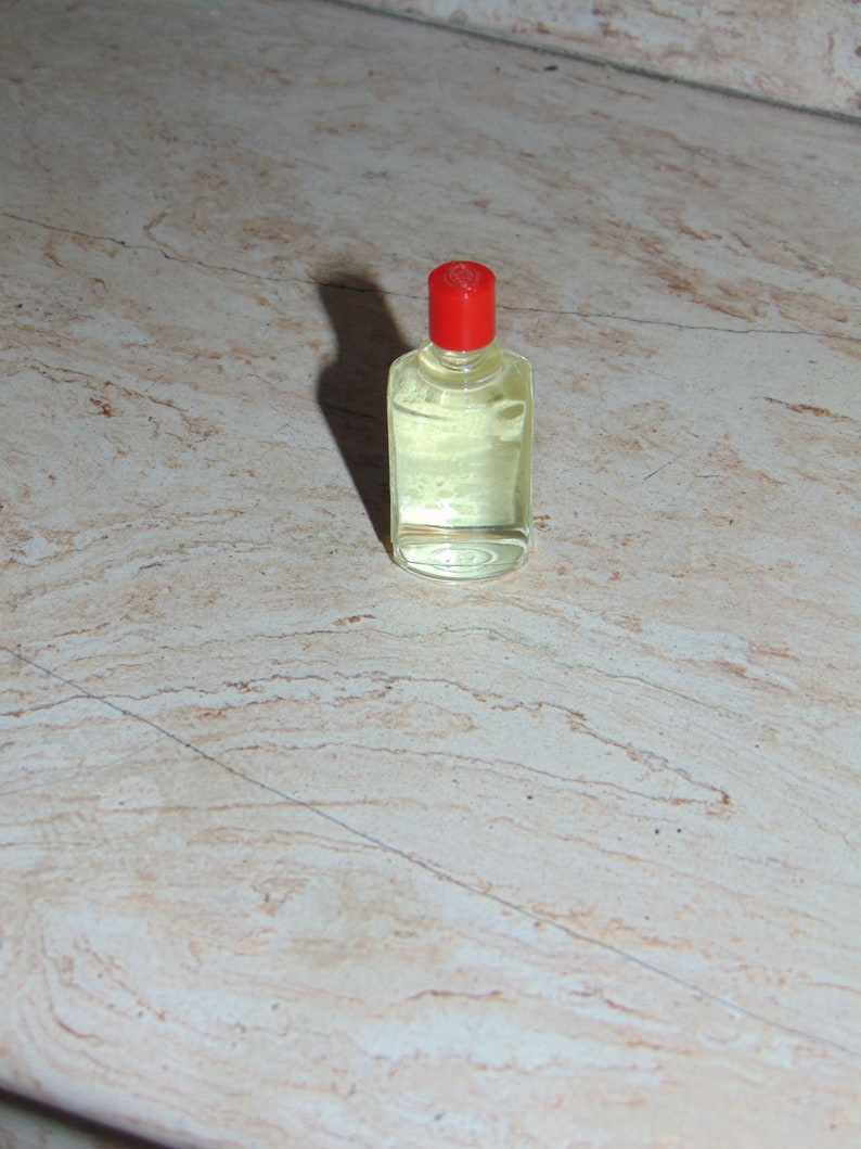 May include: A small, clear glass bottle with a red cap. The bottle is filled with a light yellow liquid.
