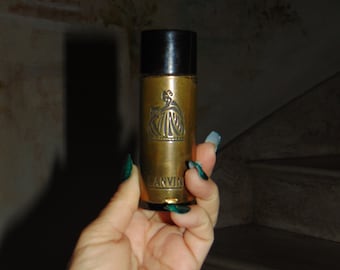 May include: A gold-colored perfume bottle with a black top. The bottle has a raised design of a woman in a dress and the word "LANVIN" is printed on the bottom.