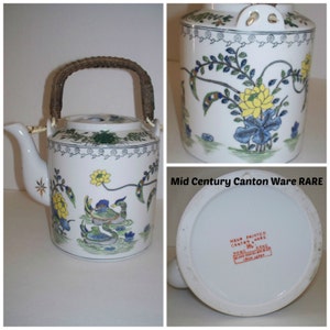 May include: A white porcelain teapot with a brown woven handle. The teapot is decorated with a floral design in shades of blue, yellow, green, and red. The bottom of the teapot has a label that reads "Hand Painted Canton Ware Hong Kong Blank Porcelain From Japan."