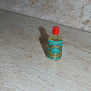 May include: A small, clear glass bottle with a red cap and a blue and gold label. The label reads "Eau de Cologne" and "4711" in a decorative font.