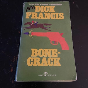 May include: A vintage paperback book titled "Bonecrack" by Dick Francis. The cover is green with orange lettering and a red illustration of a gun. A horse and rider are also depicted. The year "1971" is handwritten on the top left.