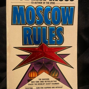 May include: A paperback book cover with a red star and the title "Moscow Rules" by Robert Moss, co-author of "The Spike". The cover features a red star with two eyes and a quote from The Washington Post.