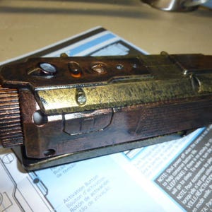 Op de afbeelding: Een close-up van een bruine en gouden camera met een getextureerd oppervlak. De camera heeft een zwarte lens en een paar knoppen aan de bovenkant.