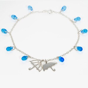 May include: A silver anklet with a delicate chain and blue glass raindrop charms. The anklet features two silver charms shaped like umbrellas.