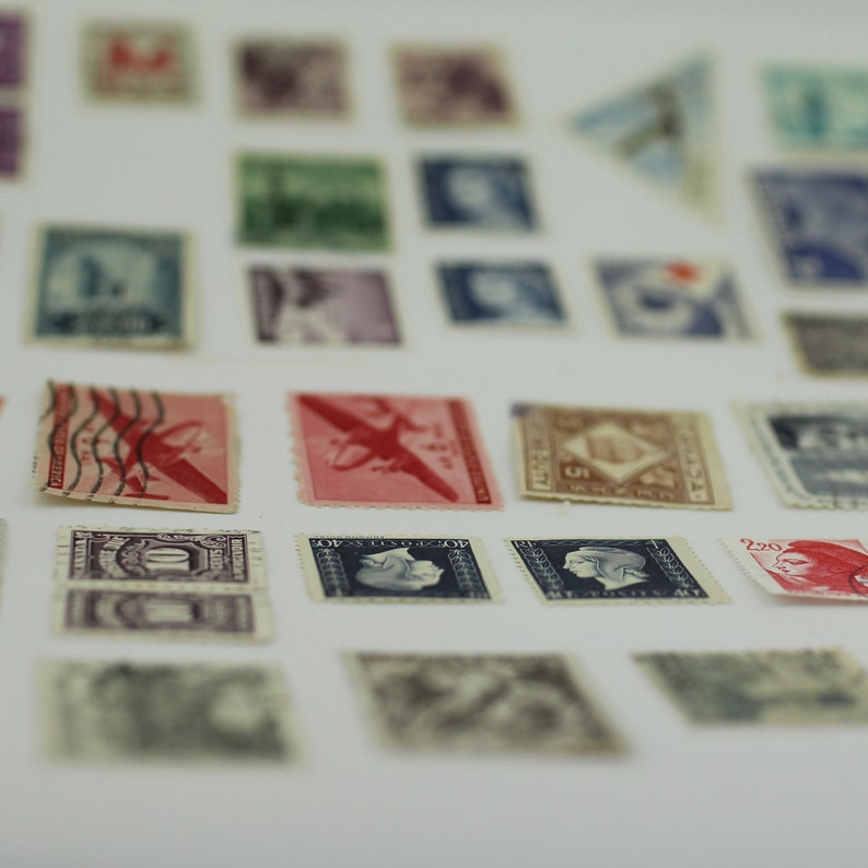 Puede incluir: Una colecci&oacute;n de sellos postales antiguos con varios dise&ntilde;os, incluyendo aviones, personas y patrones abstractos. Los sellos est&aacute;n dispuestos en filas sobre una superficie blanca.