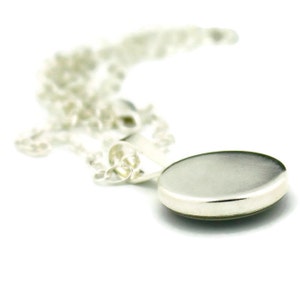 May include: A silver chain necklace with a round silver pendant. The pendant is smooth and has a slightly domed shape.