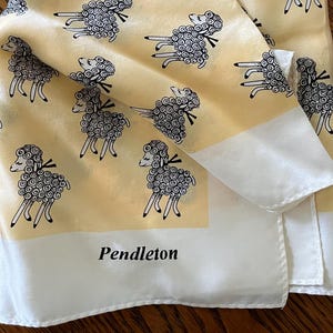 May include: A yellow silk scarf with a repeating pattern of black and white sheep. The scarf has a white border and the word "Pendleton" printed in black.