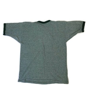 May include: A grey ringer t-shirt with a dark green trim around the collar and sleeve ends. The short-sleeved shirt is made of a soft material. The shirt is laid flat on a white surface.