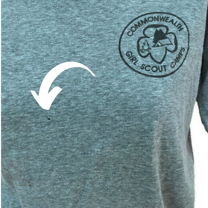 May include: A grey t-shirt featuring a black circular logo that reads "Commonwealth Girl Scout Camps". The logo includes a trefoil, a campfire, and a mountain silhouette. The shirt is made of a soft, comfortable material.