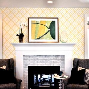 May include: A white fireplace with a gray tile surround and a black fireplace insert. Two gray armchairs with black pillows are positioned on either side of the fireplace. The wall behind the fireplace is painted a pale yellow and features a white geometric pattern.