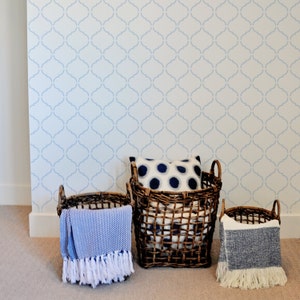 May include: Three woven baskets with blue and white patterned blankets and a pillow inside. The baskets are against a white wall with a blue patterned wallpaper.