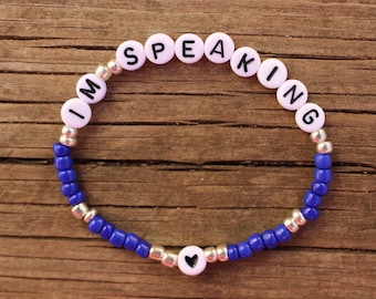 May include: A blue and silver beaded bracelet with white letter beads spelling out "I'M SPEAKING" and a small black heart charm.