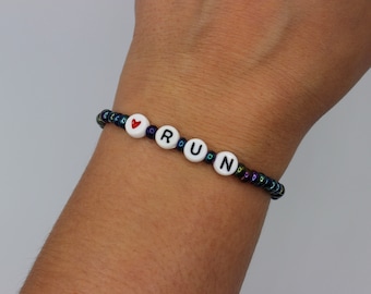 Könnte beinhalten: Ein Armband mit schwarzen und schillernden Perlen, einem roten Herz-Anhänger und weißen Buchstabenperlen, die "RUN" buchstabieren.