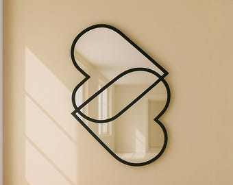 May include: A black framed mirror with two overlapping heart shapes. The mirror is reflecting a room with a window and sunlight.