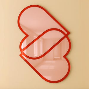 Könnte beinhalten: Zwei rote herzförmige Spiegel mit einer rosafarbenen reflektierenden Oberfläche sind an einer beigefarbenen Wand über einem Holzregal angebracht.