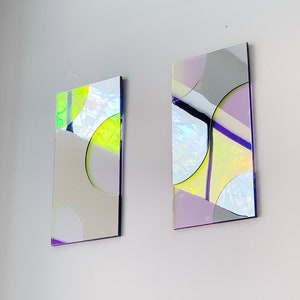 May include: Two rectangular wall art pieces with geometric shapes and iridescent colors. The pieces are made of glass and have a modern abstract design.