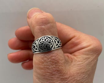 May include: A silver ring with a Celtic knot design. The ring is worn on a person's thumb.