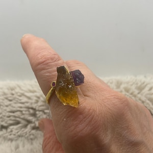 May include: Gold ring with a large, raw, yellow-brown crystal and a smaller, purple crystal.