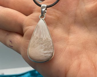 Può includere: Collana con pendente a goccia con cornice color argento. Il pendente presenta una pietra beige chiaro con motivi bianchi e piumati. La collana ha un cordino nero.