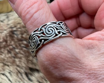 May include: Silver ring with a wide band featuring a swirling, intricate design.
