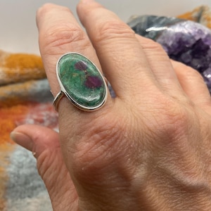 Può includere: Un anello d'argento con una pietra ovale verde e rosa incastonata in una montatura a castone.