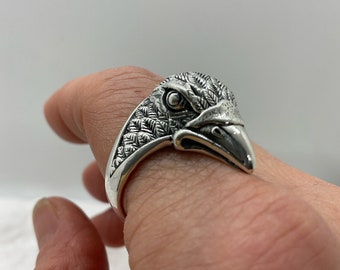 May include: A silver ring featuring an eagle head design. The eagle's head is detailed with feathers and has a sharp beak.
