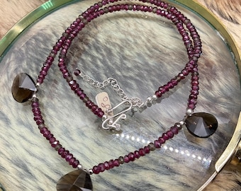 May include: A double-strand necklace made of small, dark purple beads with three teardrop-shaped, clear quartz pendants. The necklace has a silver clasp.