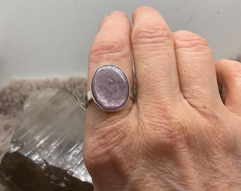 May include: A silver ring with a large, oval lavender-coloured stone. The ring has a simple, polished silver band. The stone has a smooth, polished surface and is set in a classic bezel setting.