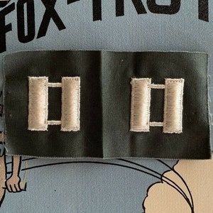 May include: A close-up of a military rank patch with two silver bars on a dark green background. The patch is labeled "Fox-Trot" and is surrounded by a cartoon illustration of a fox.