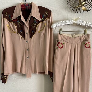 Pu&ograve; includere: Un completo in due pezzi di colore rosa chiaro. La parte superiore &egrave; una camicia a maniche lunghe con bottoni e ricami marroni sul collo e sui polsini. I pantaloni hanno vita alta e sono a gamba dritta con ricami floreali sulle tasche.