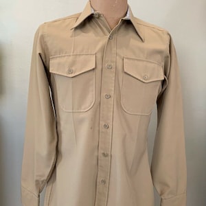 May include: A tan long-sleeved button-down shirt with two chest pockets and a collar. The shirt has a label that reads "Size 16 1/2 - 34-35".