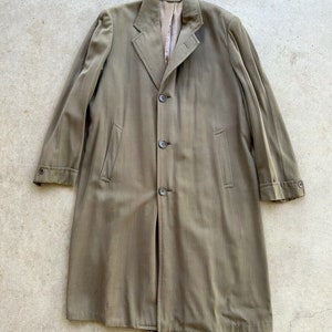May include: A long, olive-green coat featuring a notched lapel collar, a three-button front closure, and two vertical side pockets. The sleeves are finished with buttoned cuffs, and the interior is lined with a smooth, light-colored fabric.