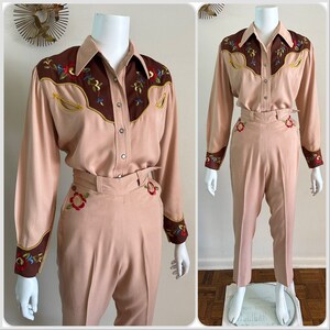 Pu&ograve; includere: Un completo rosa chiaro in due pezzi con ricami marroni e gialli. La parte superiore &egrave; una camicia a maniche lunghe con bottoni e colletto a punta. I pantaloni hanno vita alta e gamba dritta.